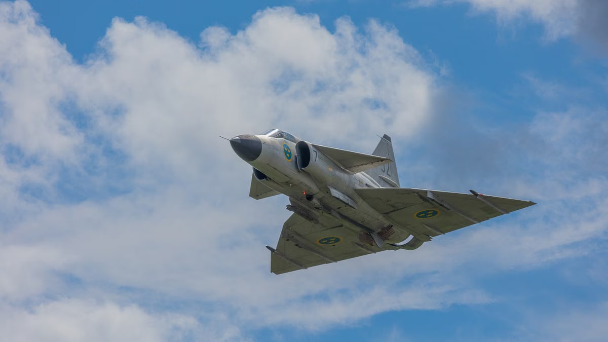 A majestic fighter jet flying through a clear blue sky, demonstrating speed and power against fluffy white clouds.